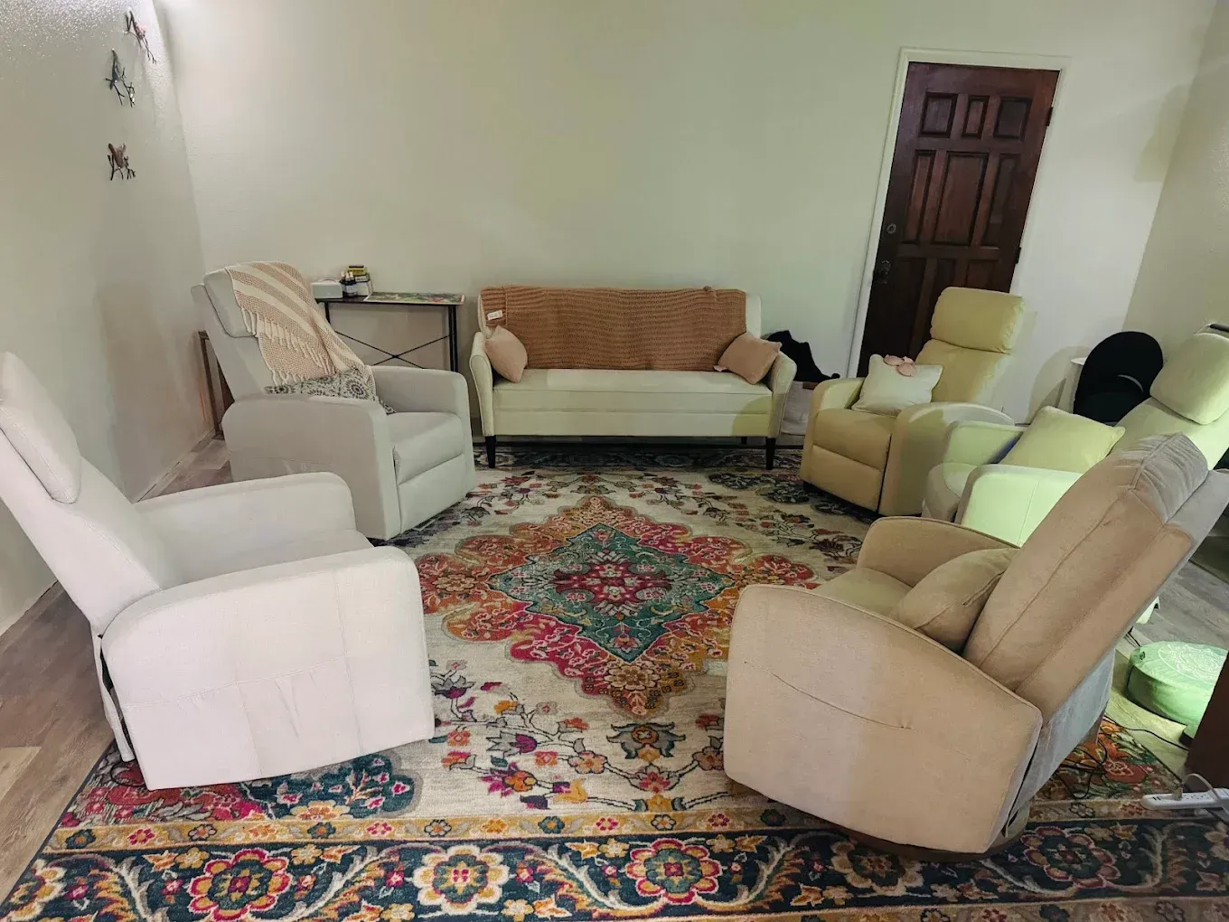 Living room with assorted armchairs, sofa, ottoman, and patterned rug around a wooden door