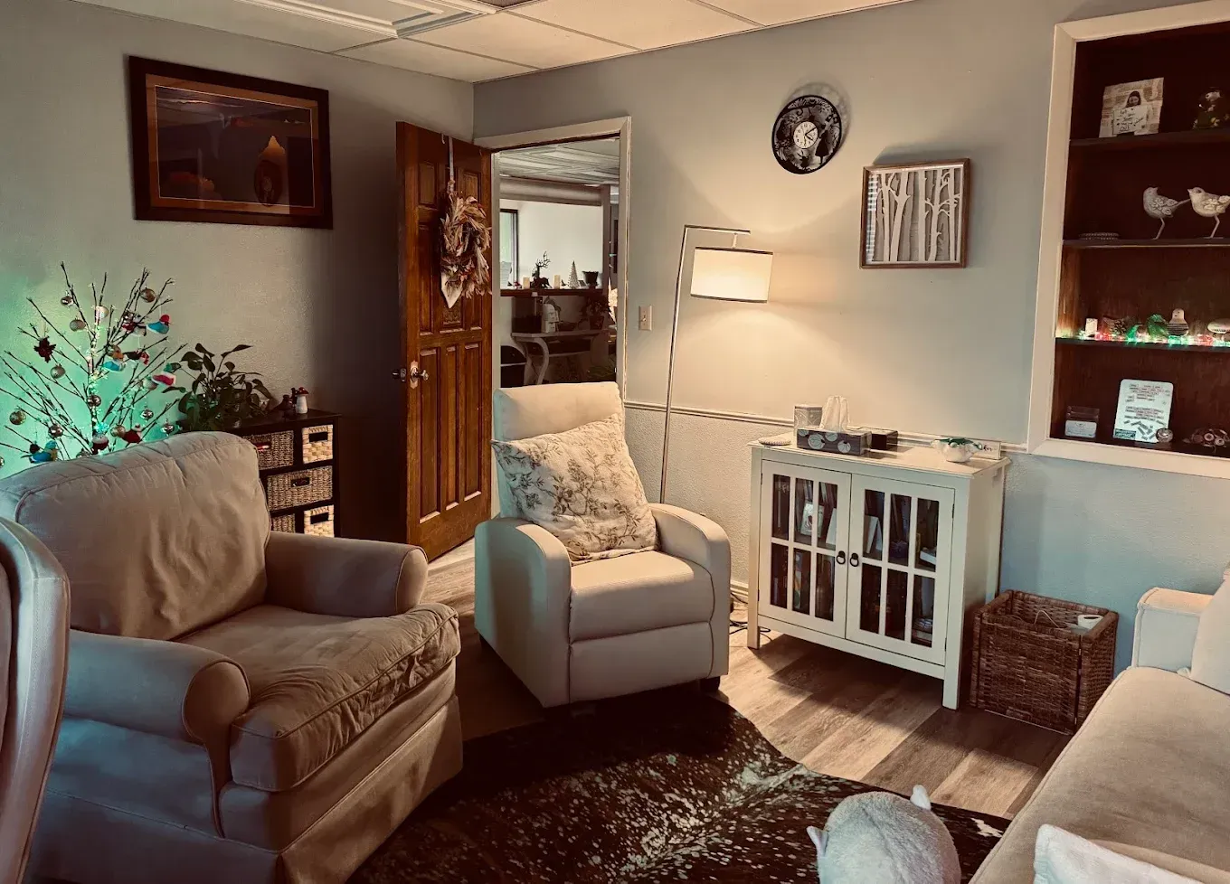Cozy living room with beige armchairs, open door, small white cabinet, and wall decor.