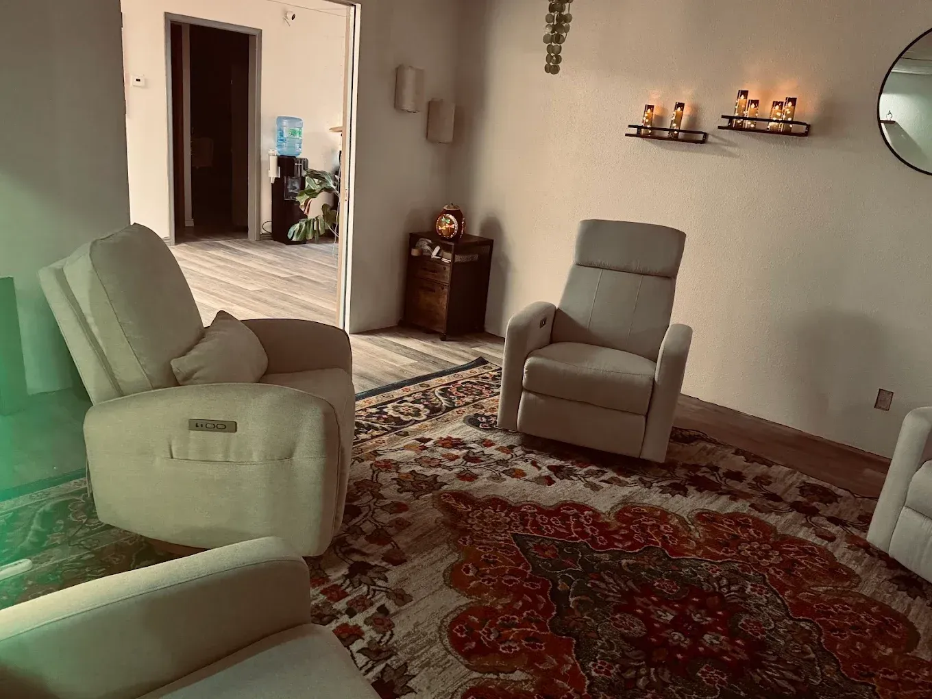 Living room with white recliners, red patterned rug, and open doorway in the background