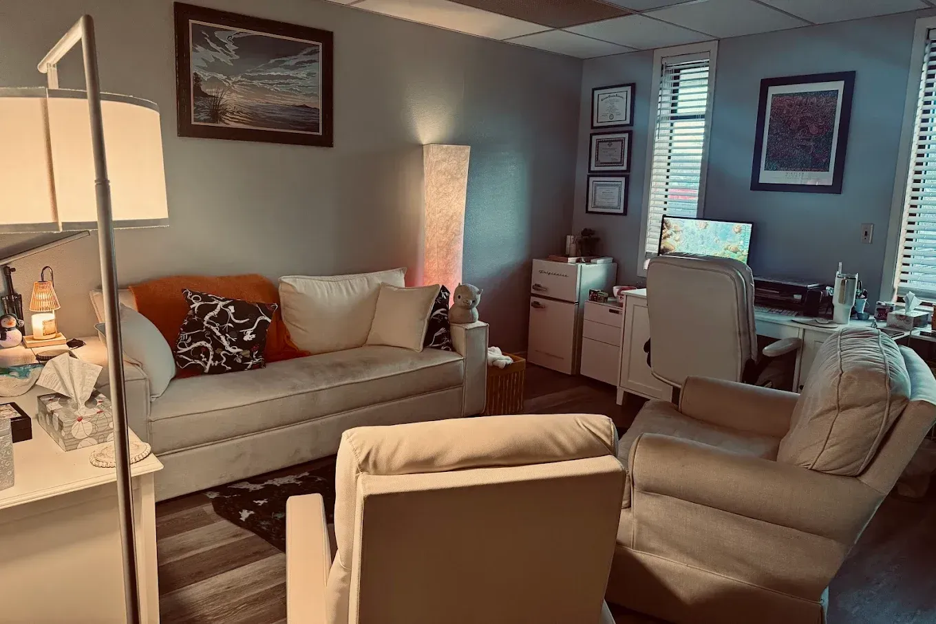 Cozy living room with beige sofas, lamp, framed art, and a view of a patio outside the window