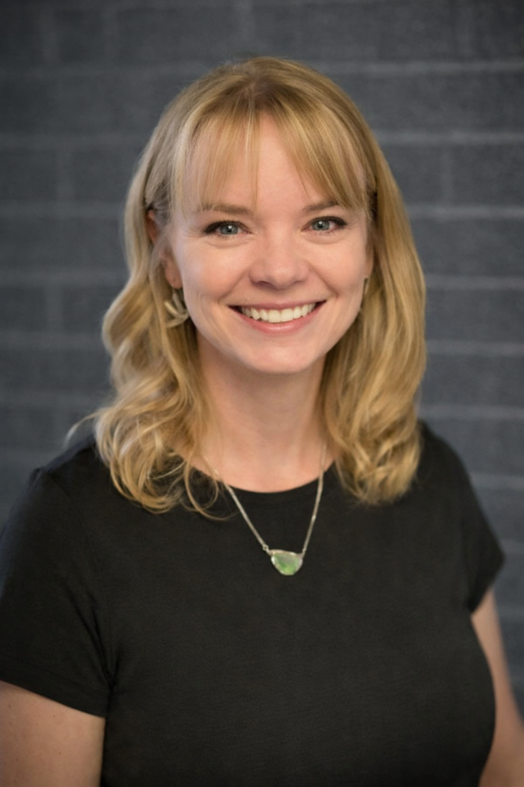 Smiling person with blonde hair in a black shirt against a gray background