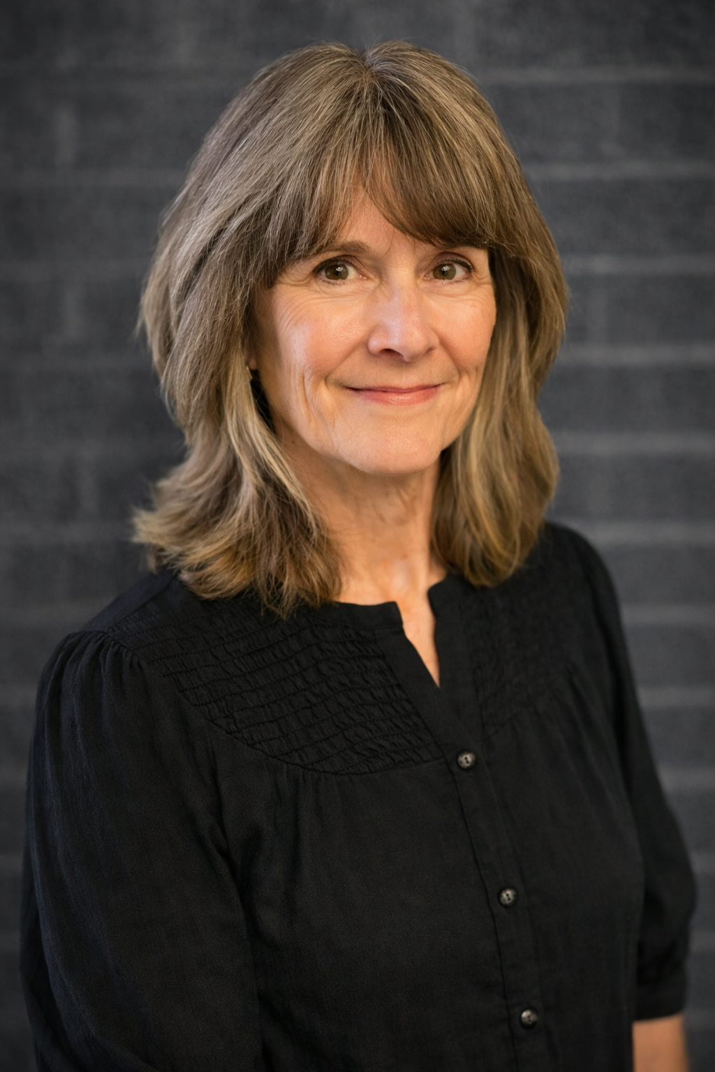 Portrait of a woman with shoulder-length gray hair wearing a black blouse against a dark gray background