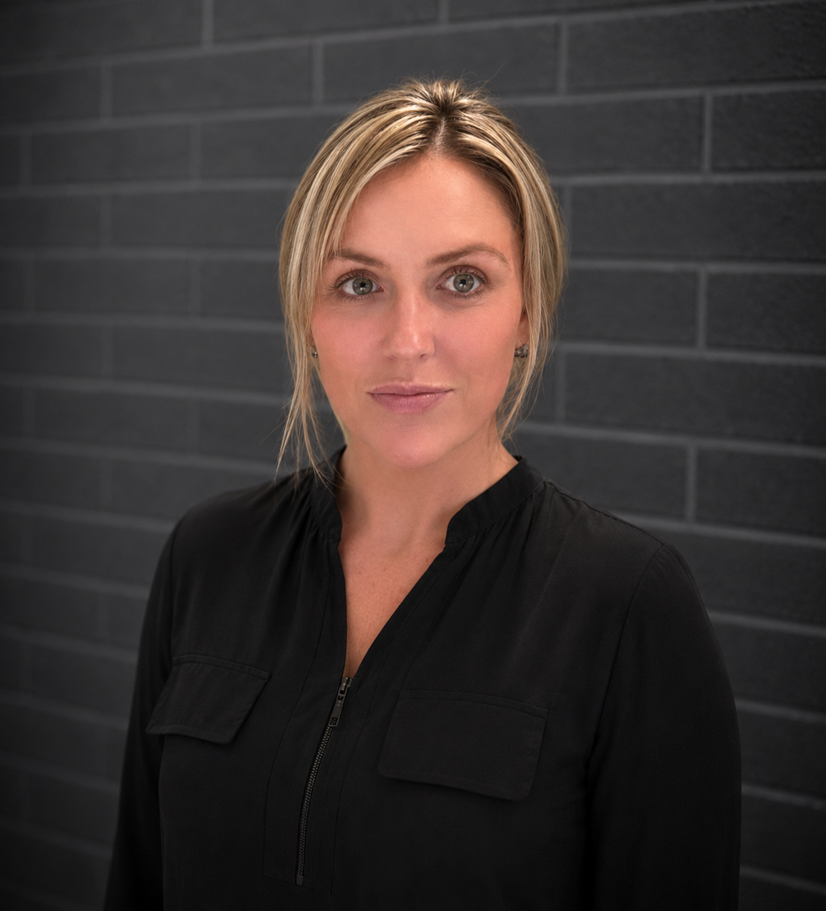Portrait of a woman in a black top standing against a dark tiled wall