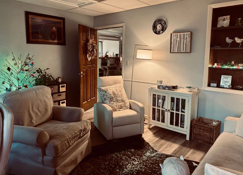 Cozy living room with beige chairs, lamp, open door, wall art, and a white cabinet.