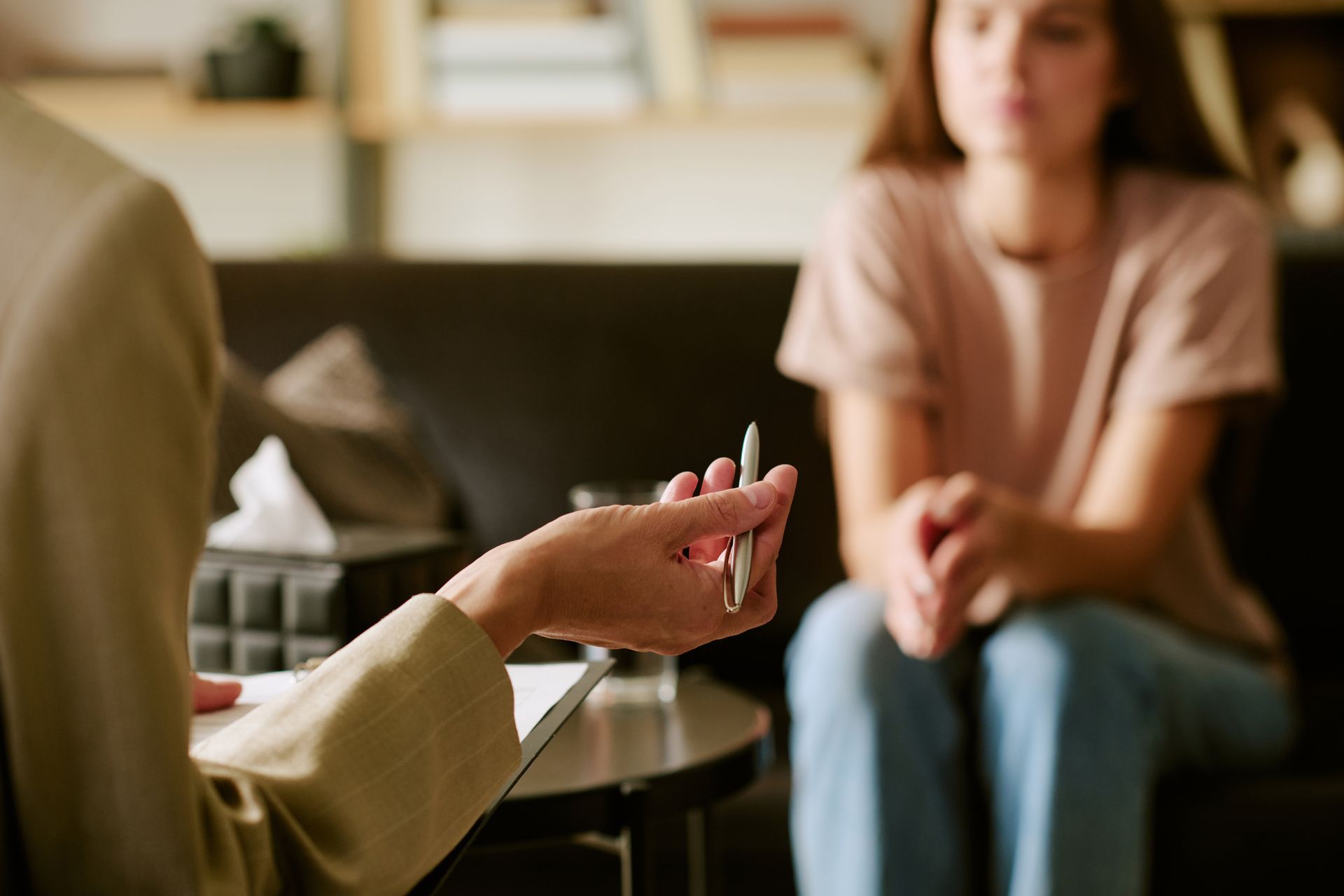 Counselor holding a pen in a therapy session with a seated client in a softly lit room