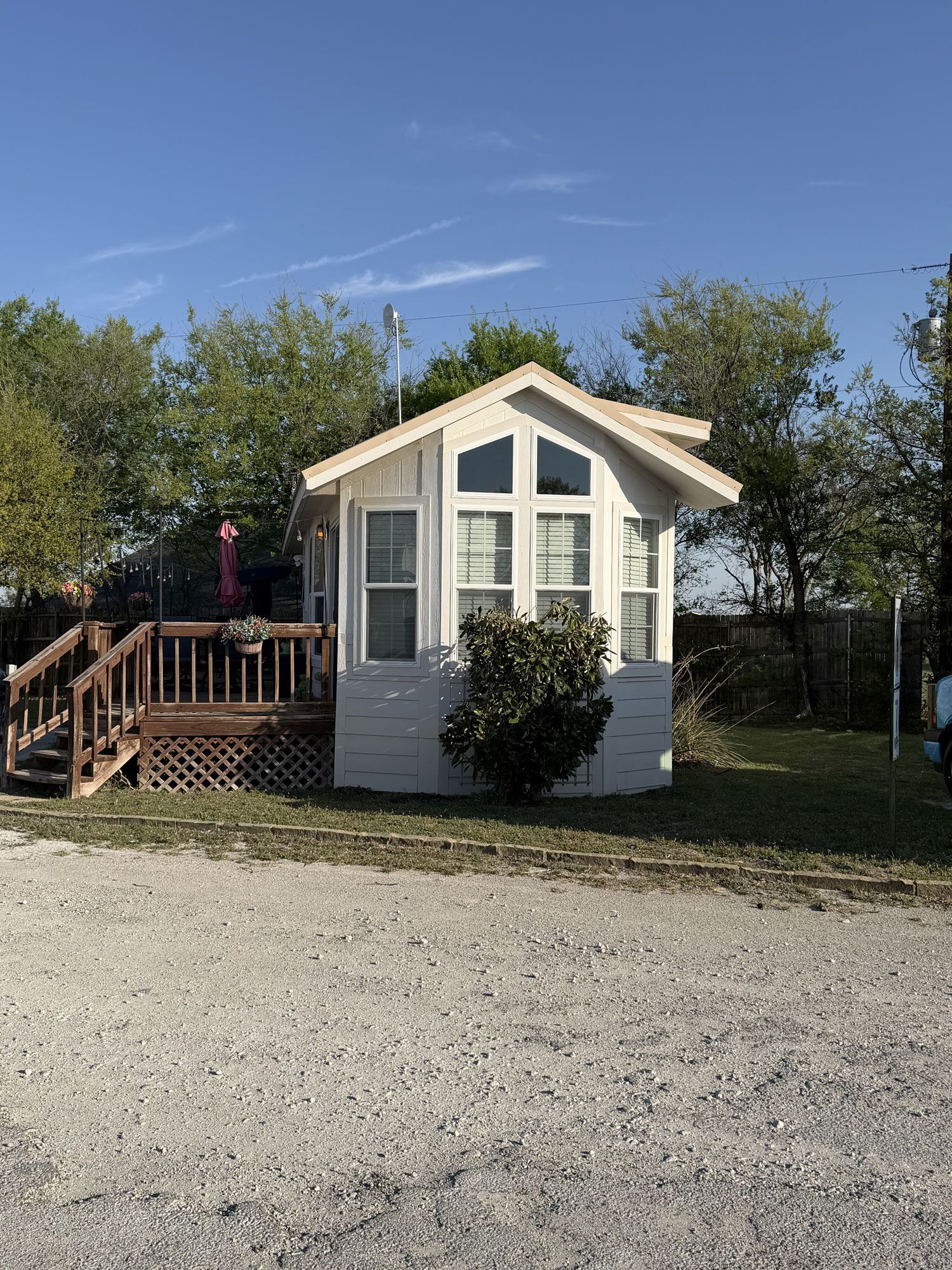 Small white cabin with a porch and steps, set beside a gravel road under a clear blue sky.