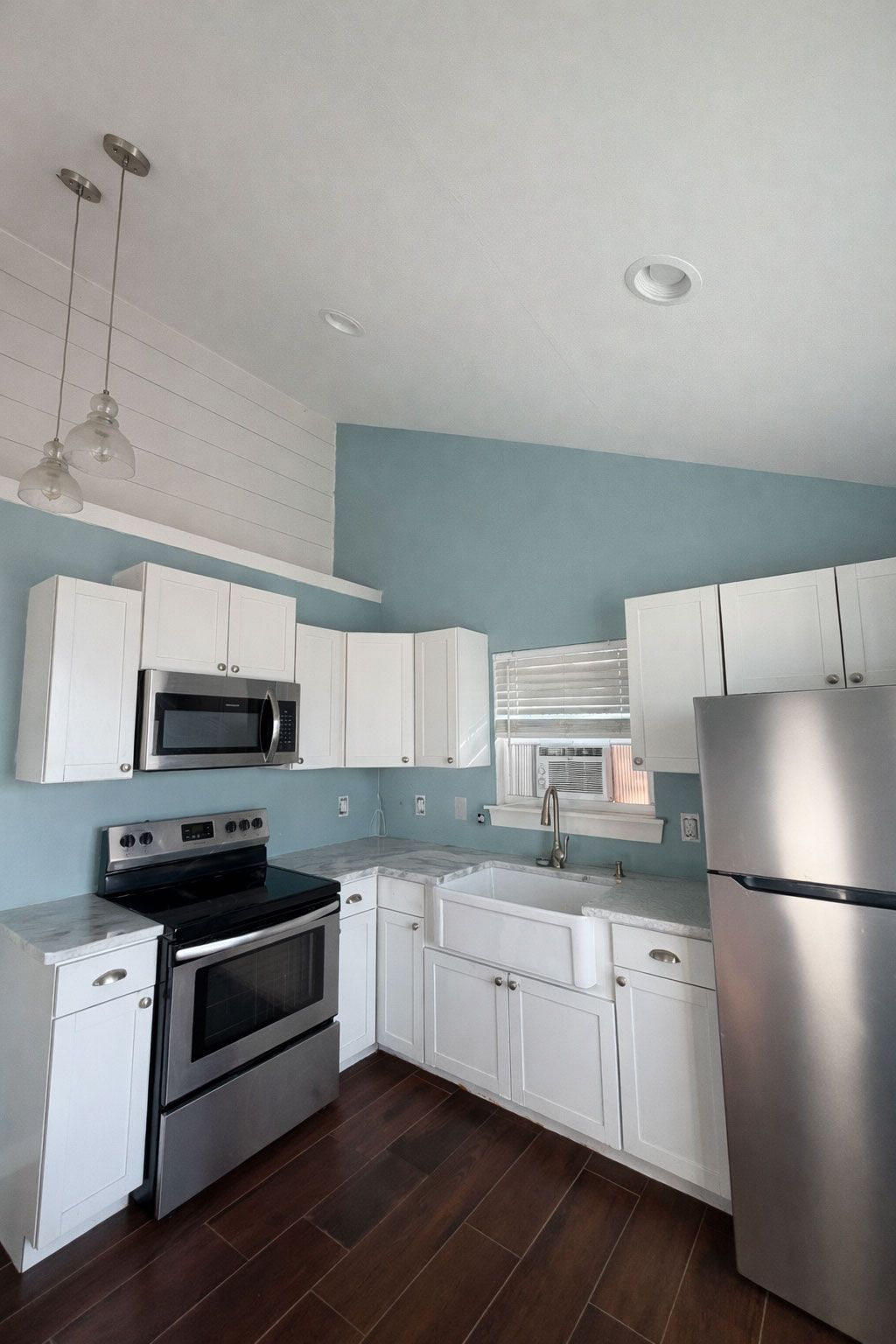 Bright kitchen with white cabinets, stainless steel fridge, black stove, and pale blue walls.