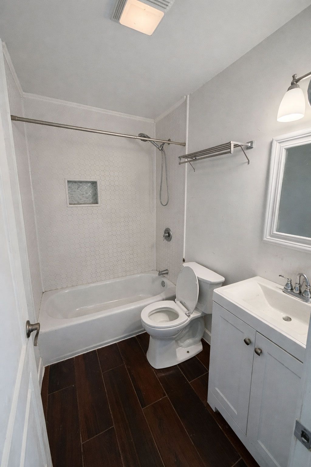 Small bathroom with a tub, toilet, sink vanity, and mirror, featuring dark wood floor and light gray walls