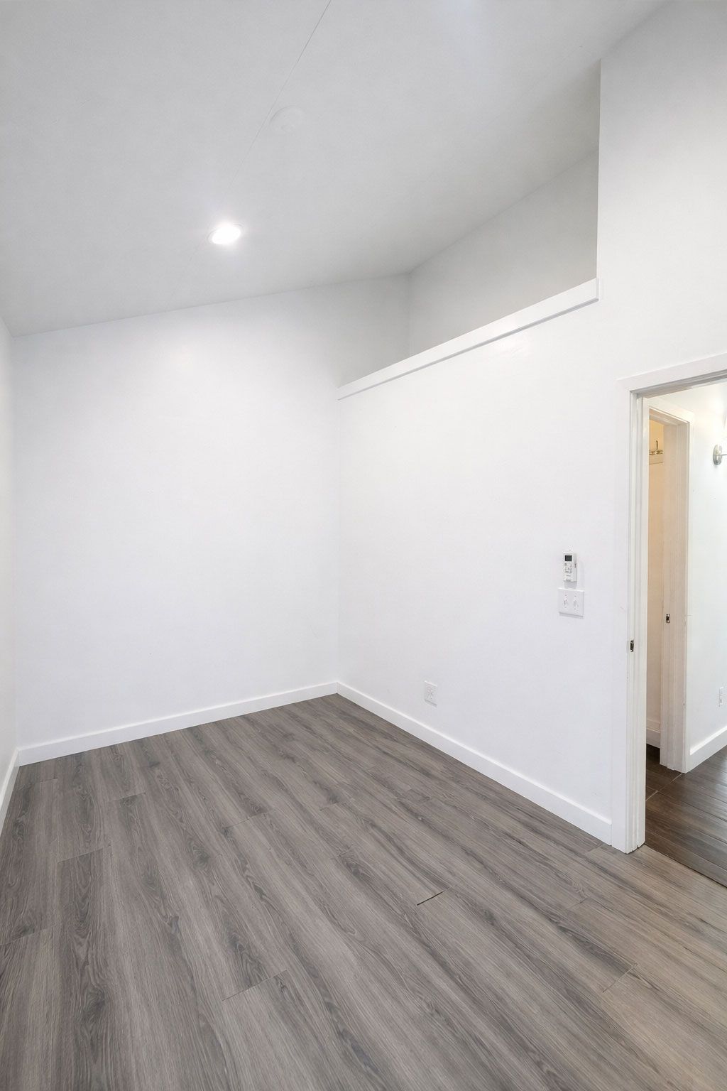 Empty white room with gray wood flooring and a doorway on the right