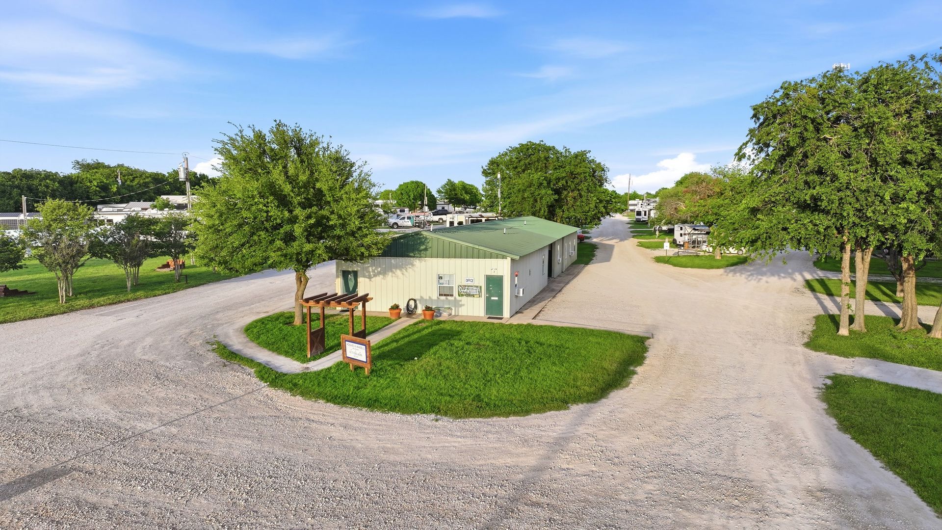Gravel driveway leading to a small white house with green lawn and trees on a sunny day