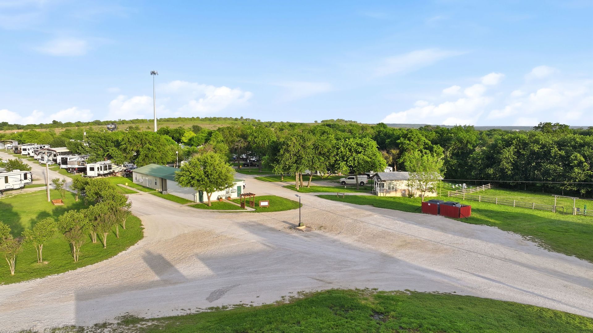Curved driveway through a green campground with cabins, trees, and a red car under a bright sky