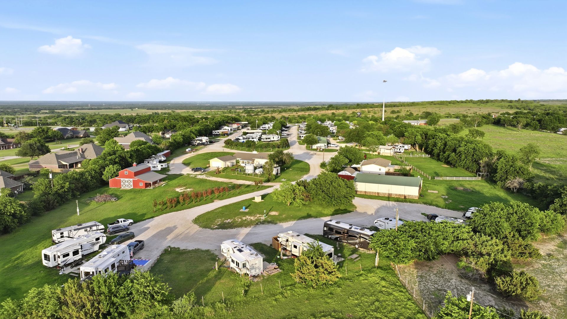 Aerial view of a rural RV park with scattered trailers, green fields, and trees under a bright sky