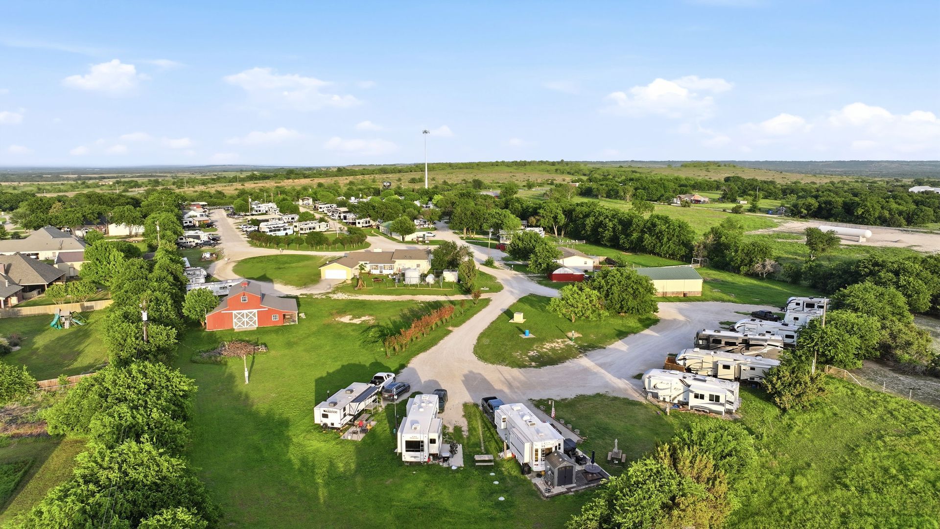 Aerial view of a RV campground with cabins, trailers, and green fields under a clear sky.