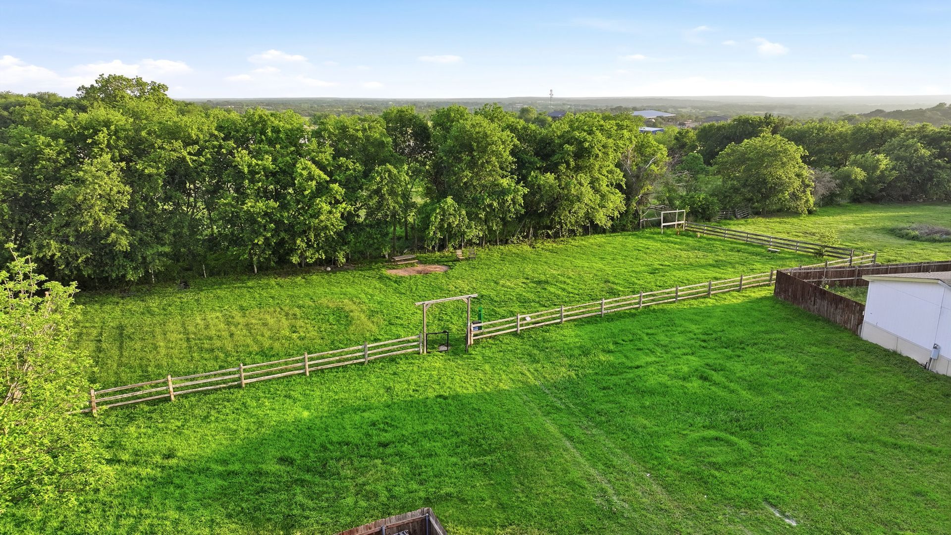 Green backyard with fenced lawn, trees, and a distant horizon under a clear sky