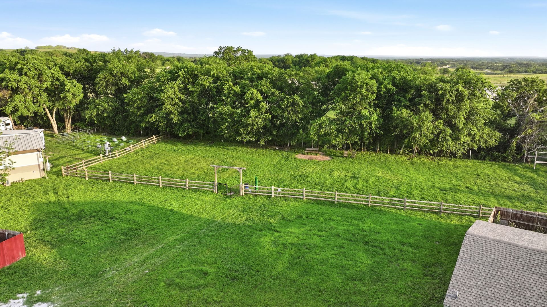 Wide green lawn bordered by trees under a bright sky, viewed from a building balcony