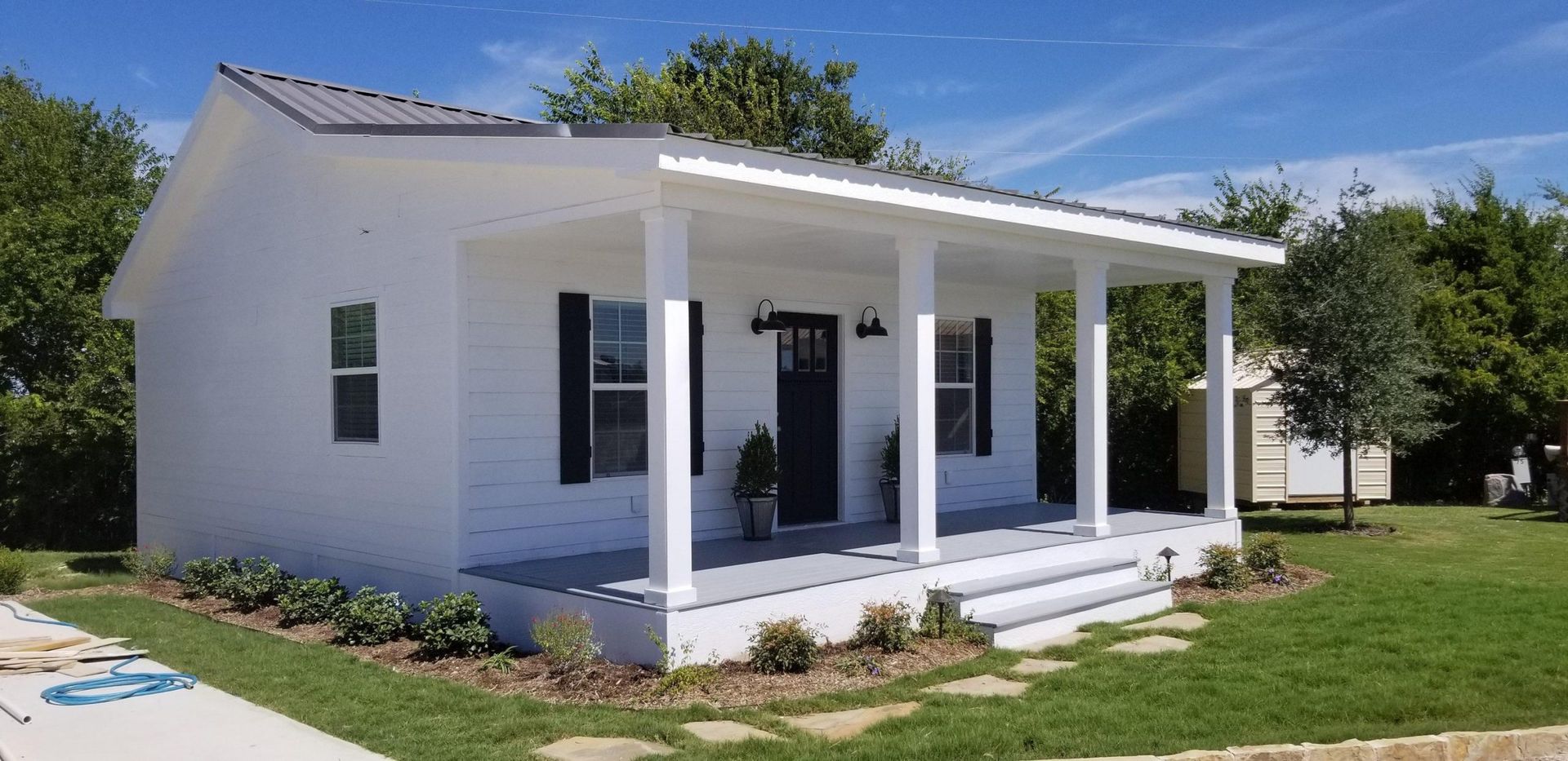 White house with porch and black shutters, on a green lawn under a blue sky.
