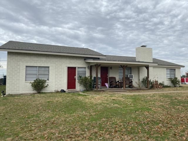 Light-colored single-story house with red doors and a covered porch on a cloudy day.