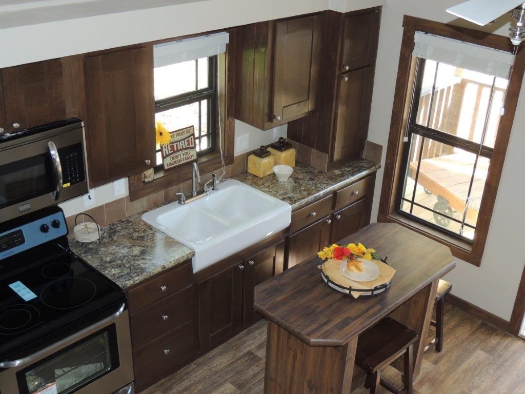 A small kitchen with dark wood cabinets, granite countertops, and a white farmhouse sink. An island sits in the foreground.