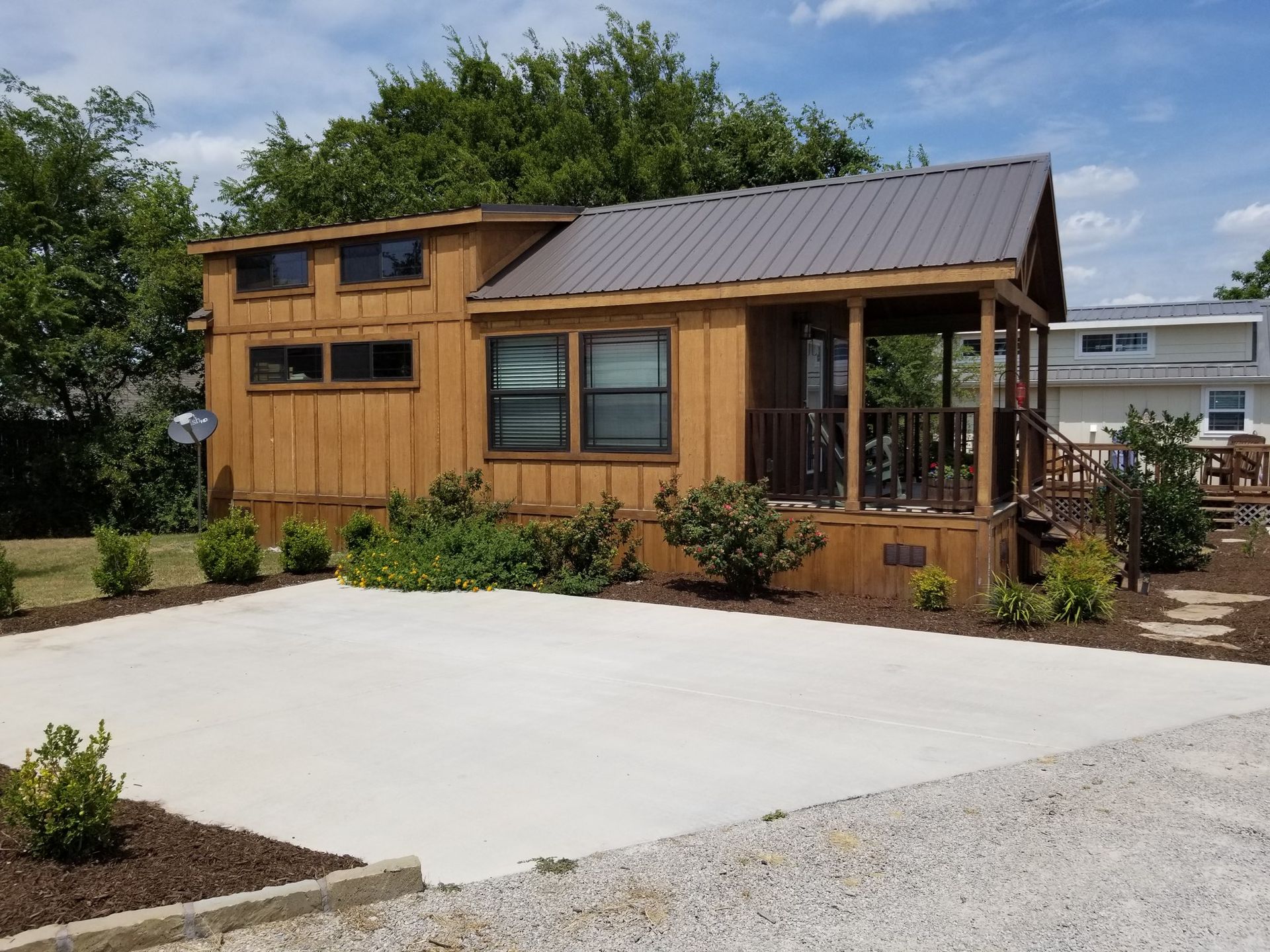 Tiny brown cabin with a metal roof and a porch, set on a concrete pad.