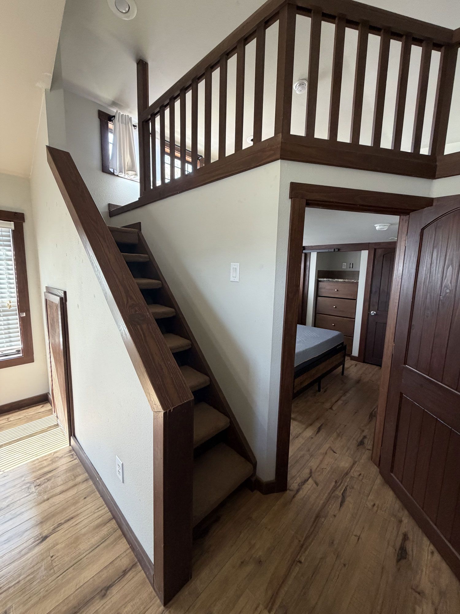 Small home loft with wooden stairs, railing, and an open bedroom below.