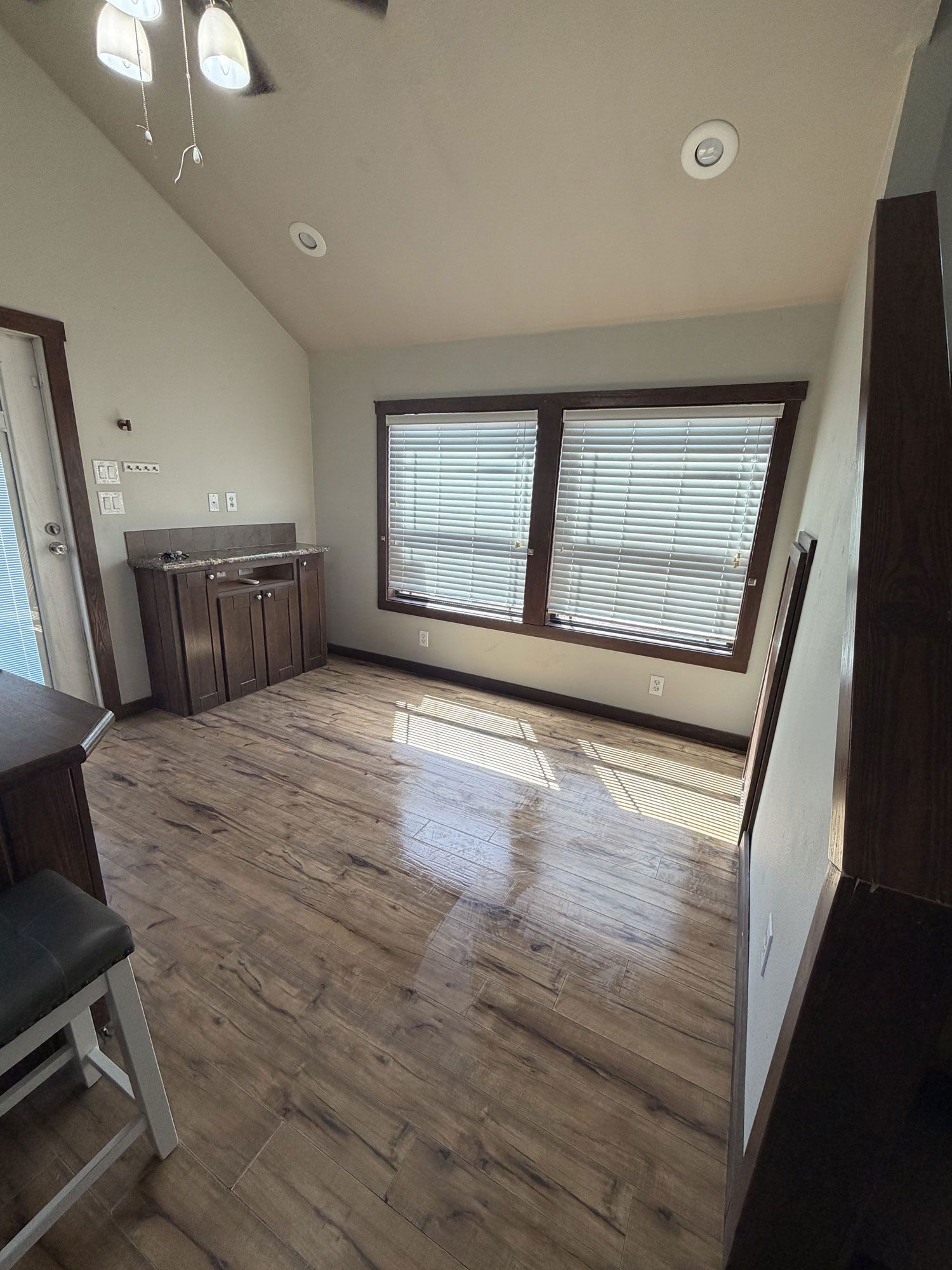 Empty room with wood floor, large window blinds, and a small cabinet under a slanted ceiling.