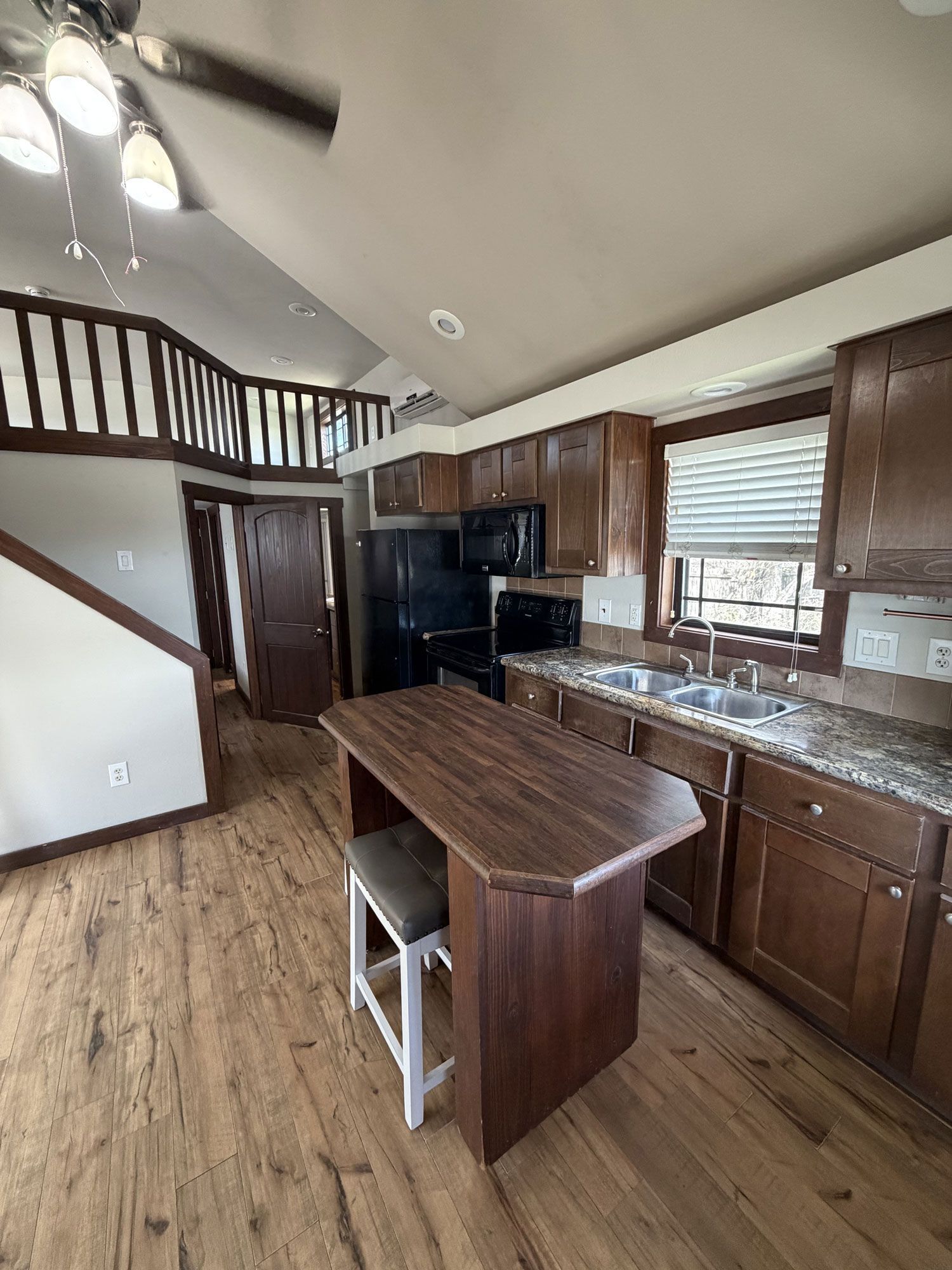Open kitchen with wood cabinets, island, staircase, and high ceilings with ceiling fan.