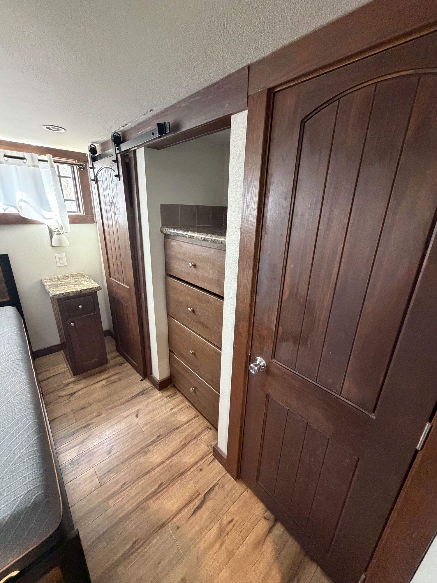 Narrow hallway with wooden floors, open closet, dresser, and a door in a small room.