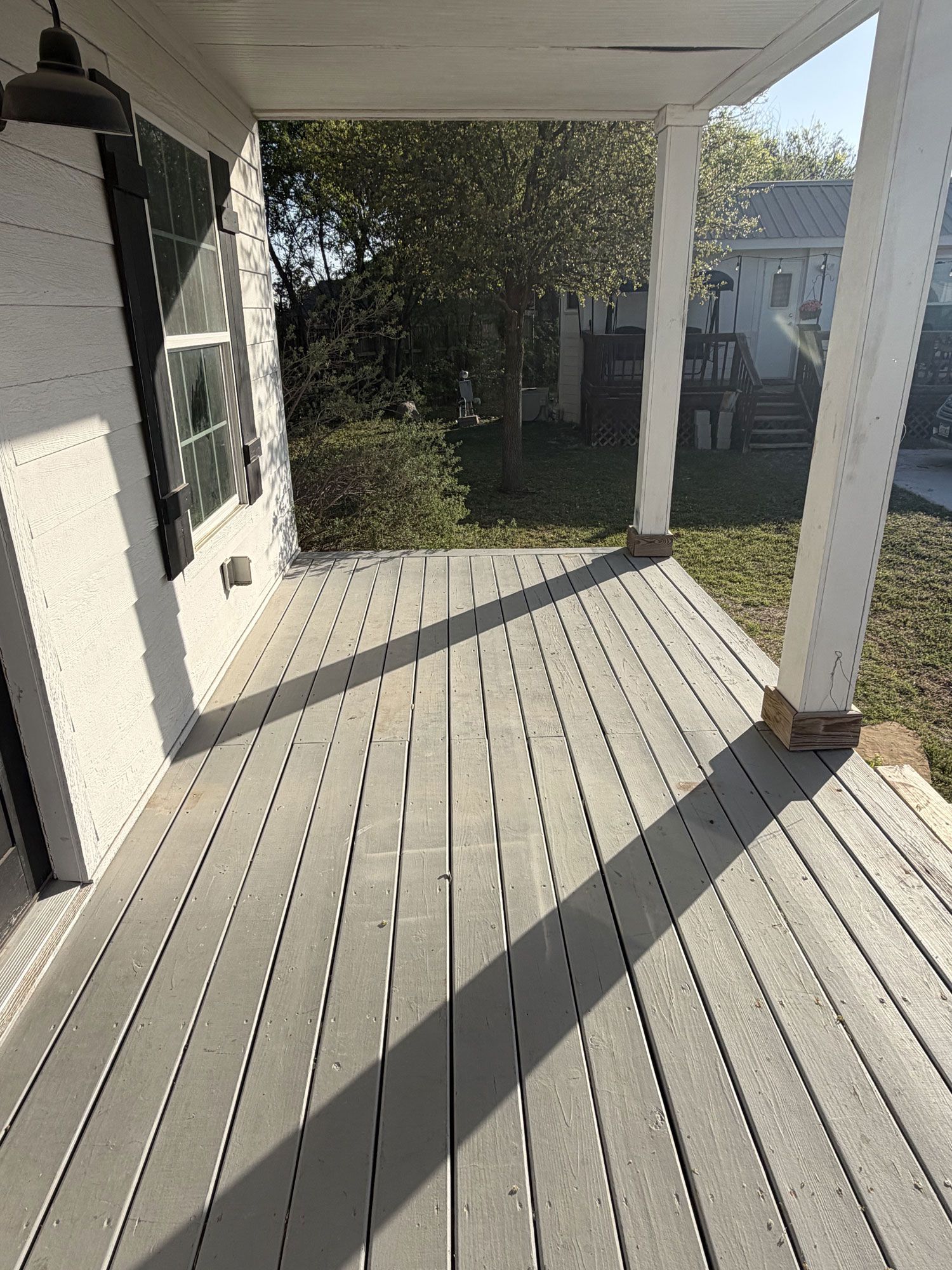 Covered porch with white railings and pillars, striped sunlight on the floor, and a yard beyond.