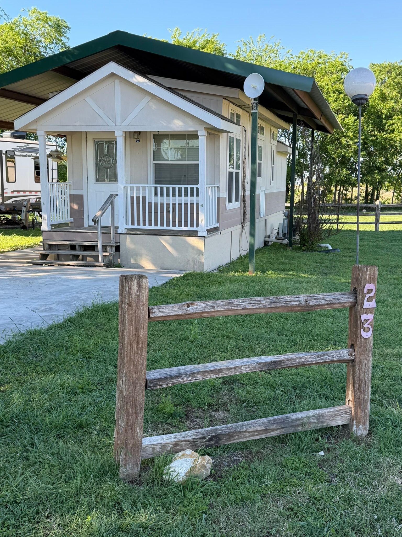 Small white cottage with porch, green roof, and wooden fence in a grassy yard under sunny skies.