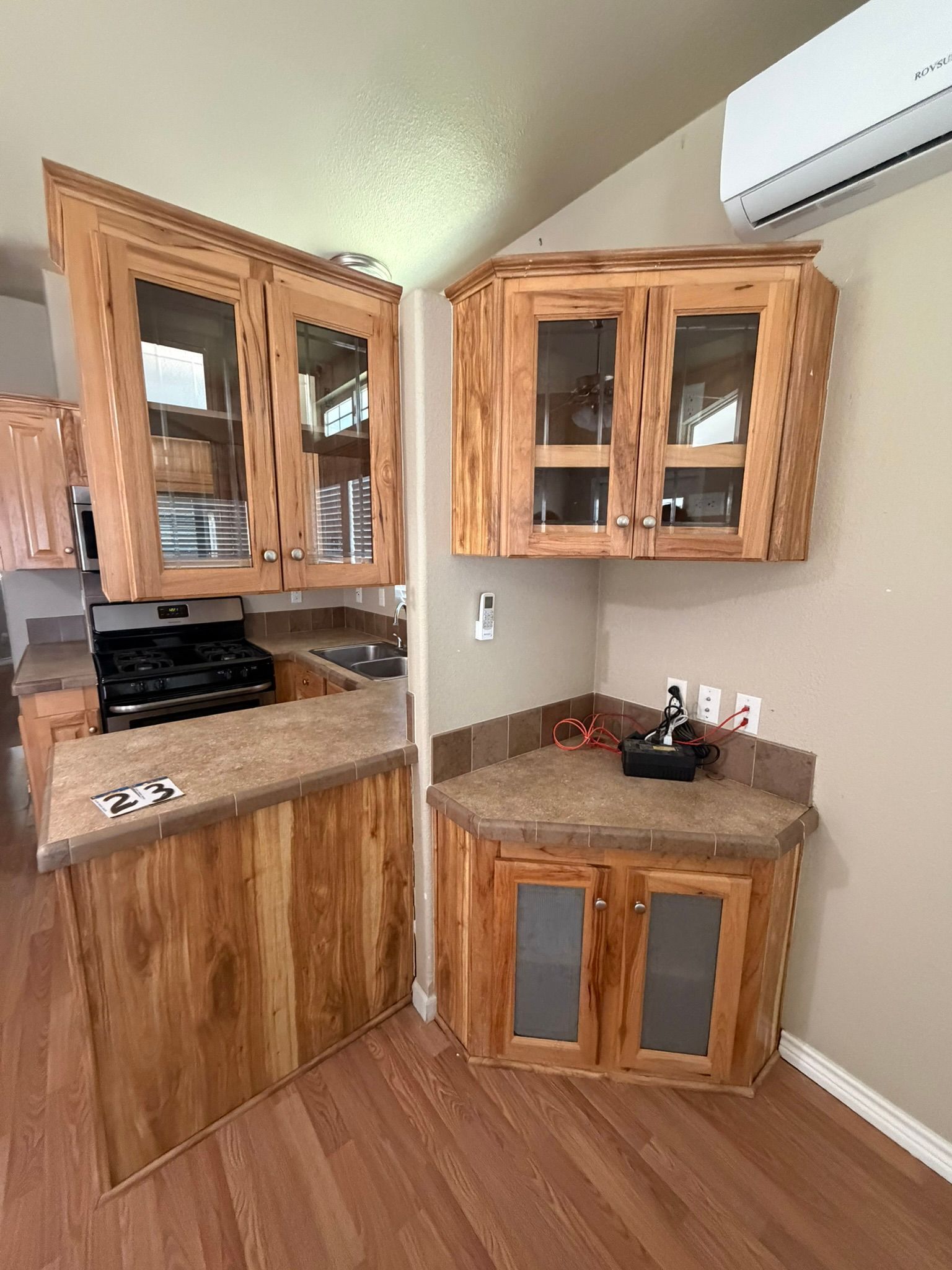 Compact kitchen corner with wood cabinets, brown countertops, and an air conditioner above.