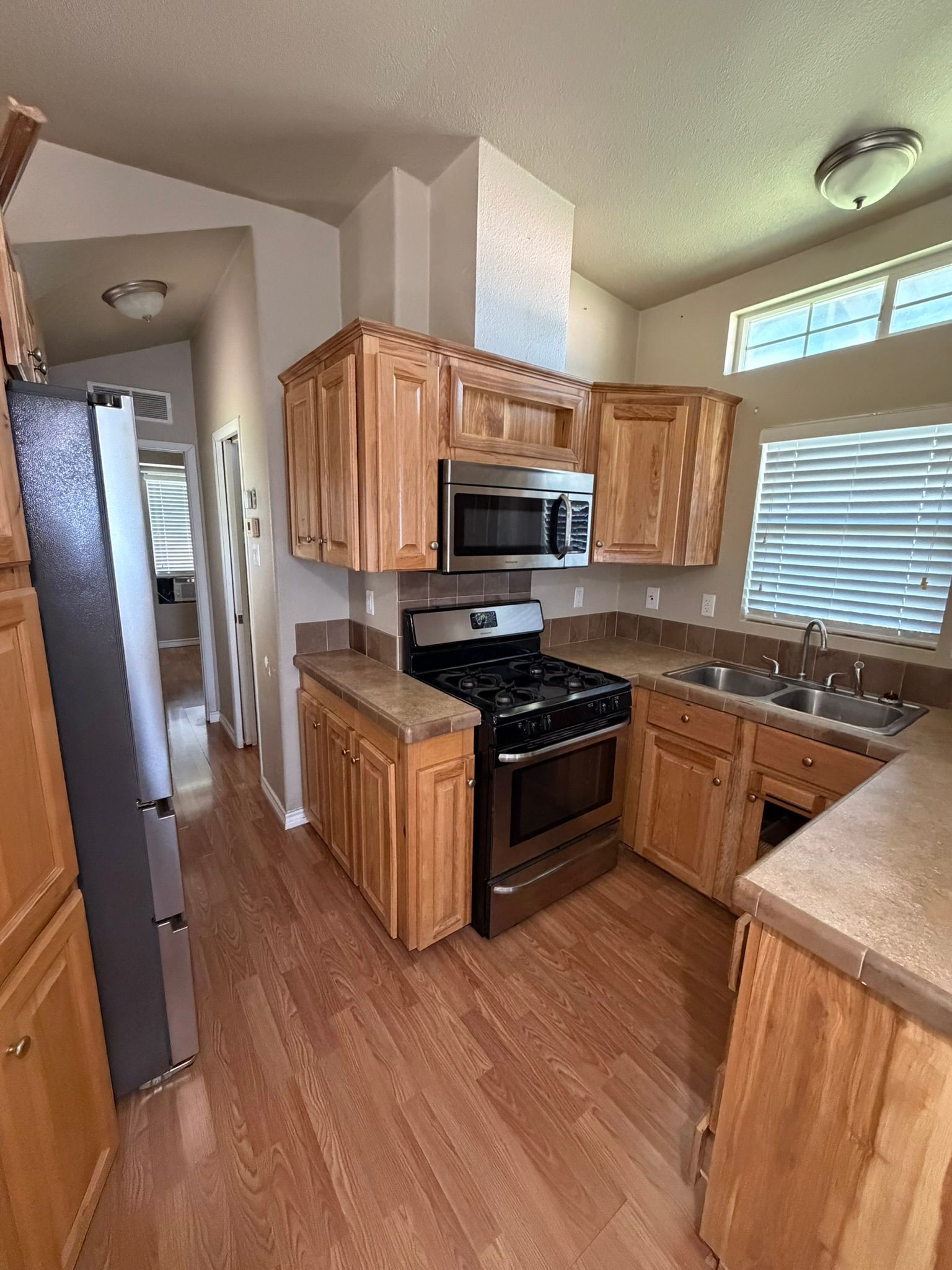 Small kitchen with wood cabinets, black stove, stainless fridge, and window blinds letting in light.