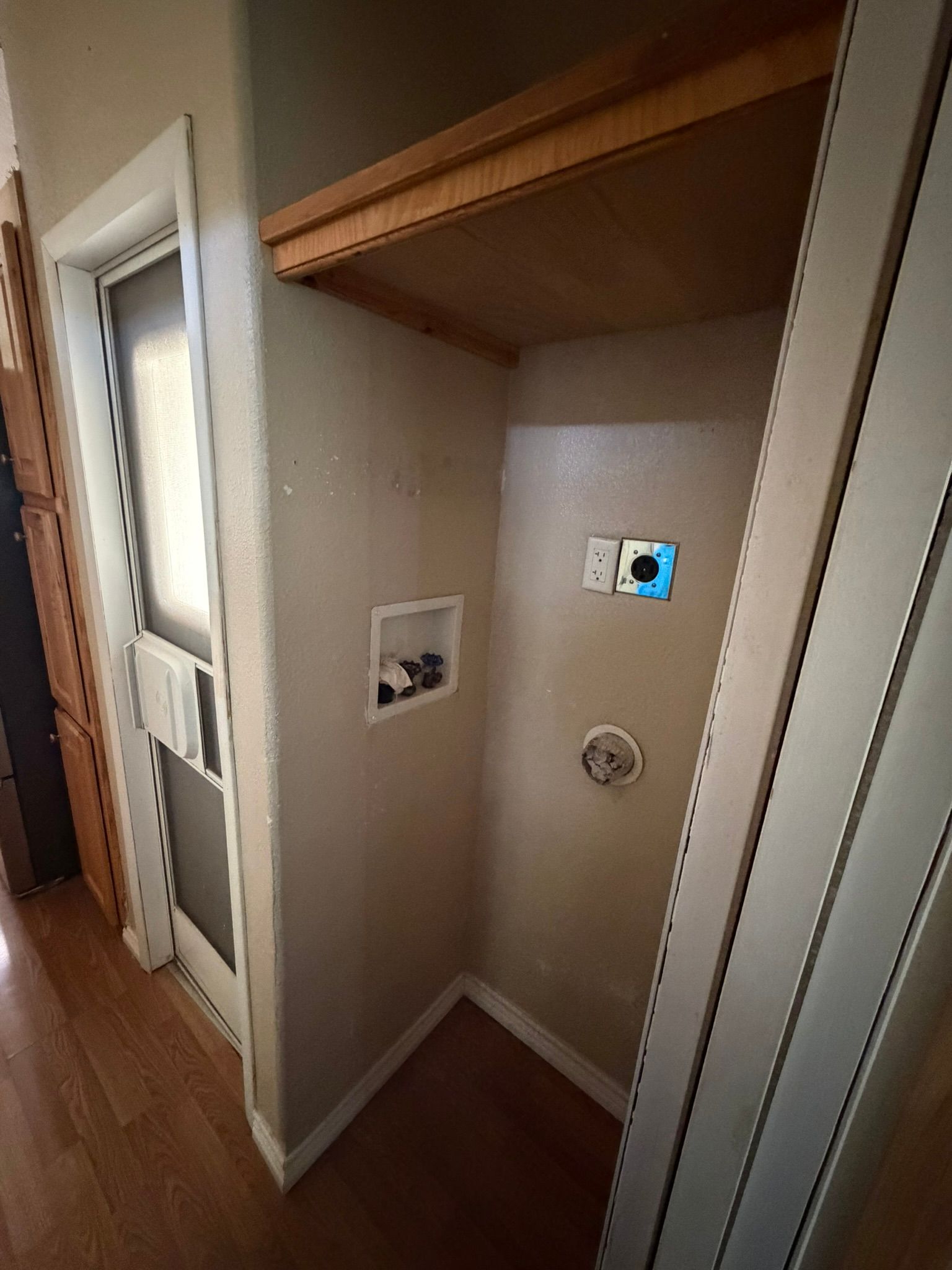 Empty laundry closet with hookups, shelf, and closet door opening into a hallway