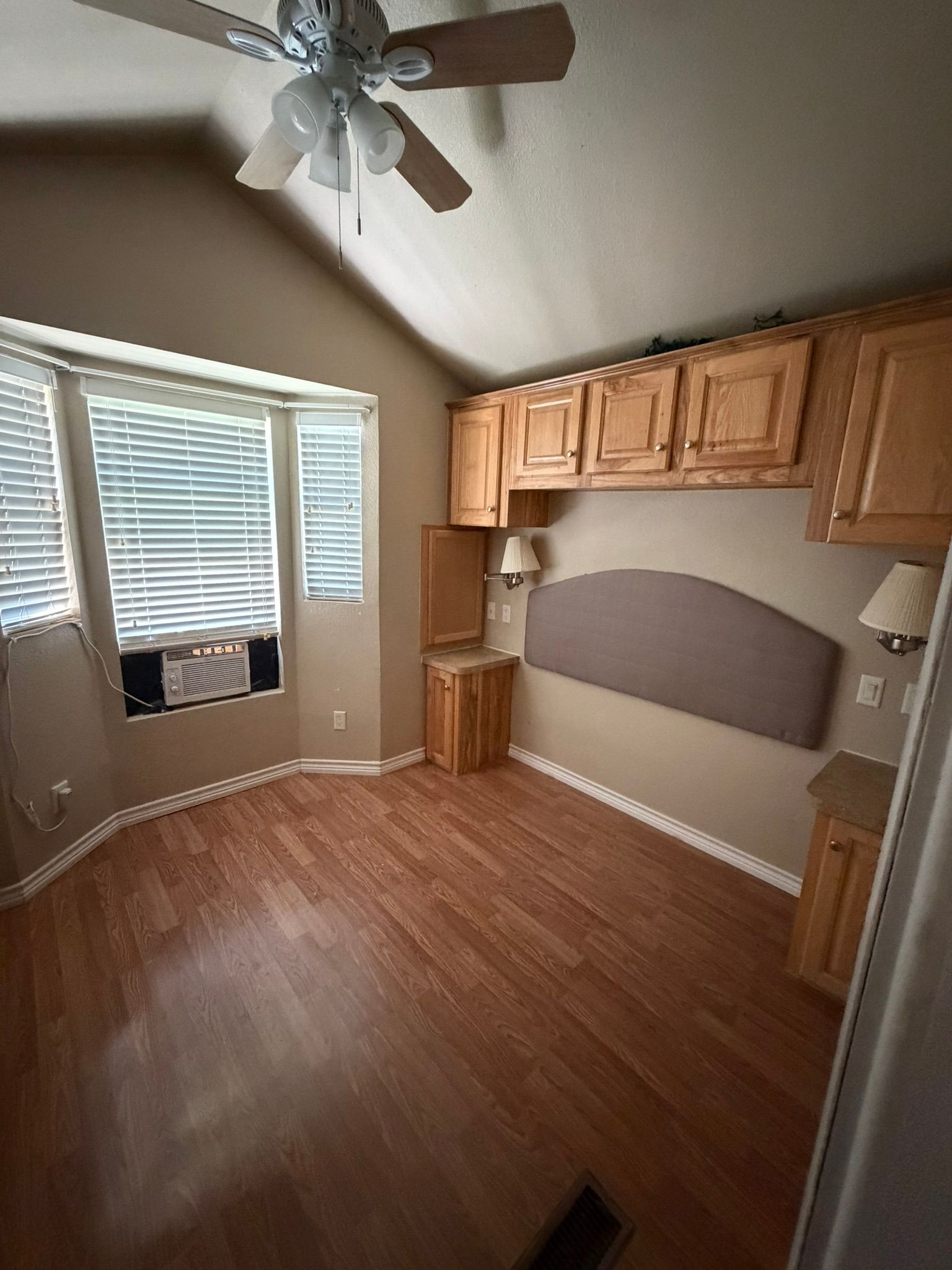Empty bedroom with wood floors, bay window, ceiling fan, built-in cabinets, and a desk nook.