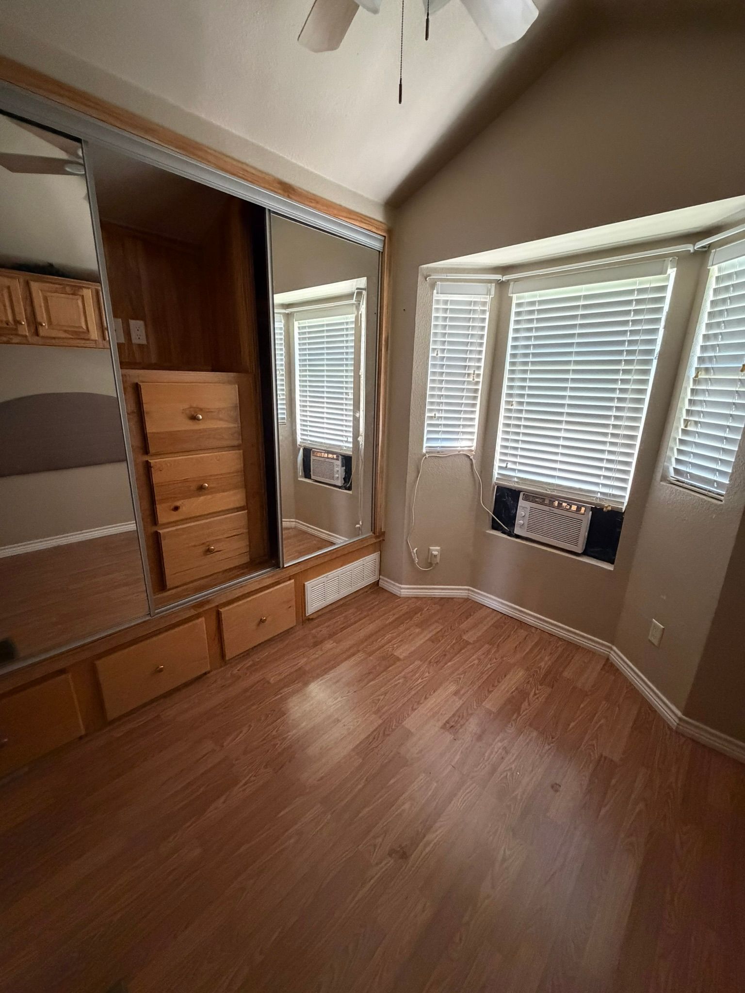 Empty bedroom with hardwood floors, built-in wooden closet, and two windows with blinds.