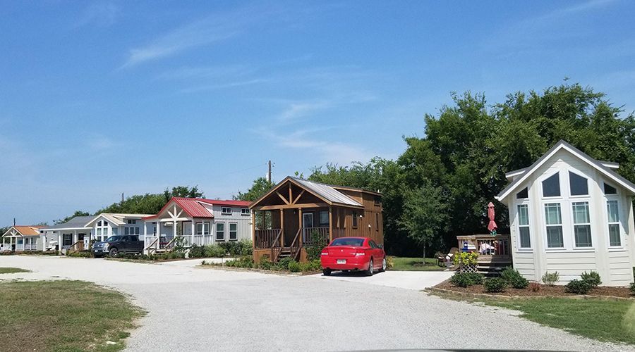 A row of colorful tiny houses on a gravel road under a blue sky, with one red car parked in front.