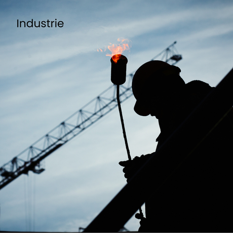 Silhouette d'un ouvrier soudant au chalumeau sur un chantier de construction, grue en arrière-plan, ciel bleu.