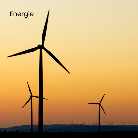 Des éoliennes se découpent sur un coucher de soleil aux teintes orangées et jaunes. Le mot « Énergie » figure en haut à gauche.