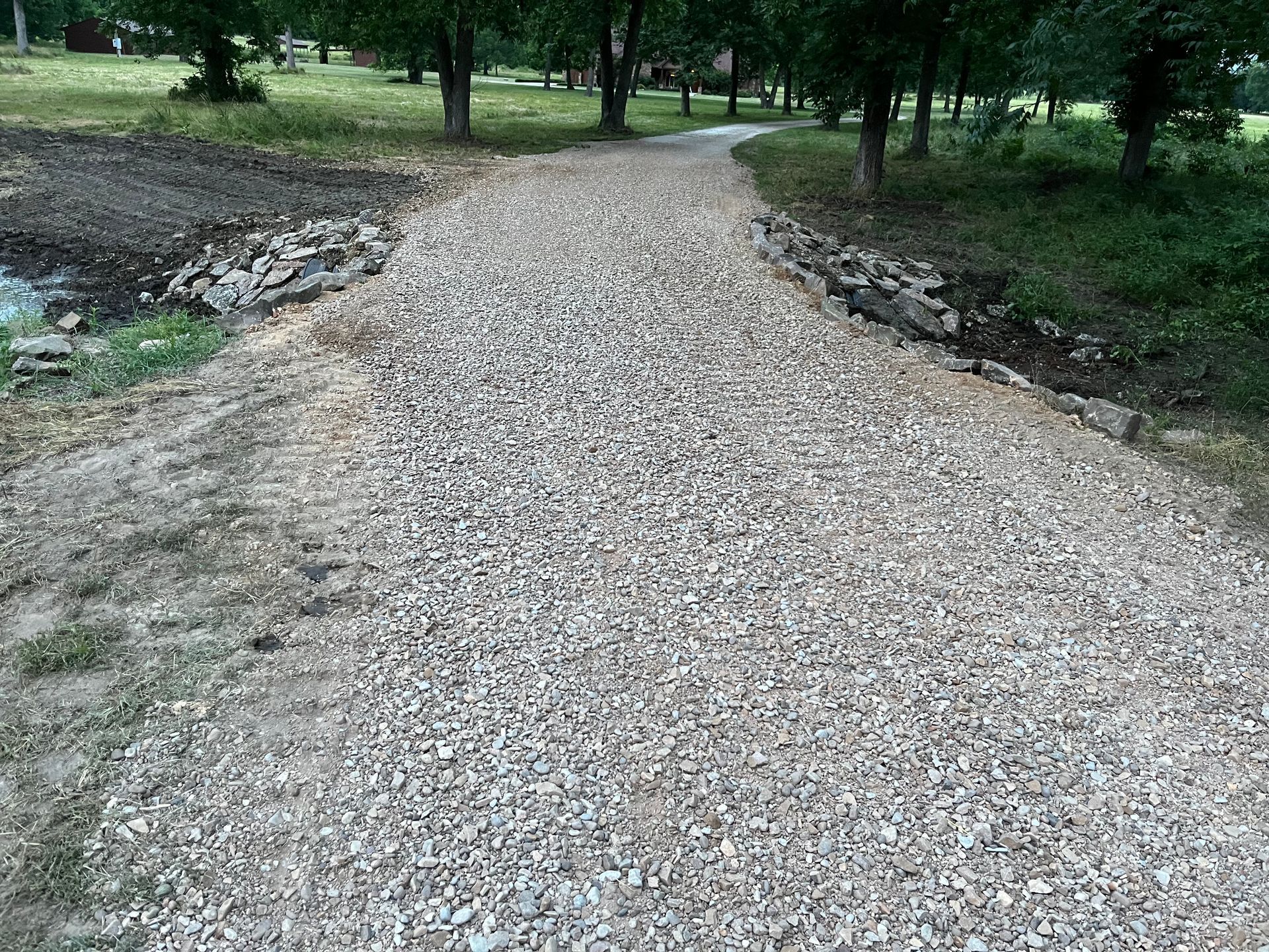 Gravel pathway through a park, trees line the sides.