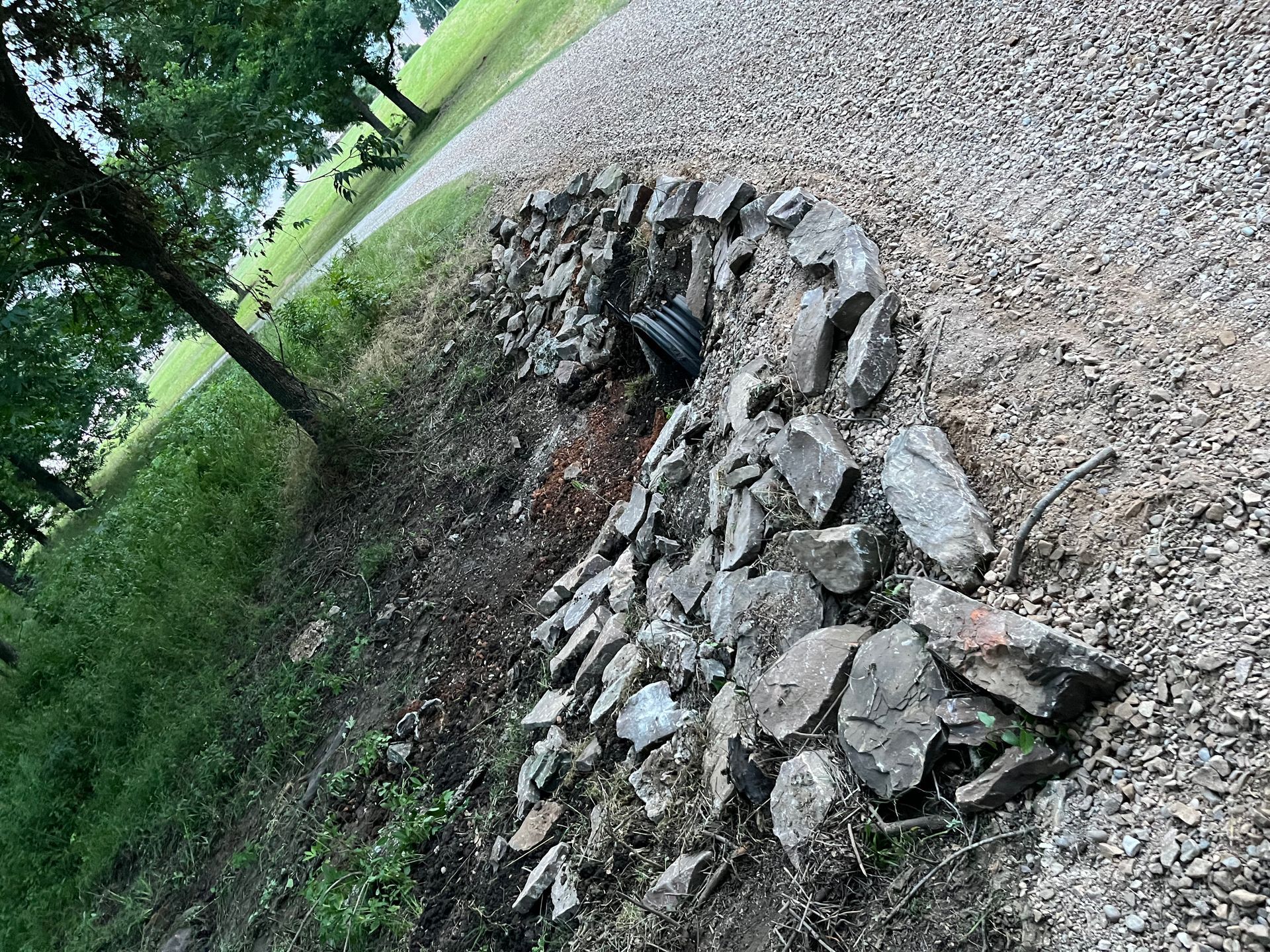 Stone wall with drainage pipe along a gravel driveway.