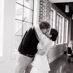 A bride and groom are kissing in a hallway in front of a window.