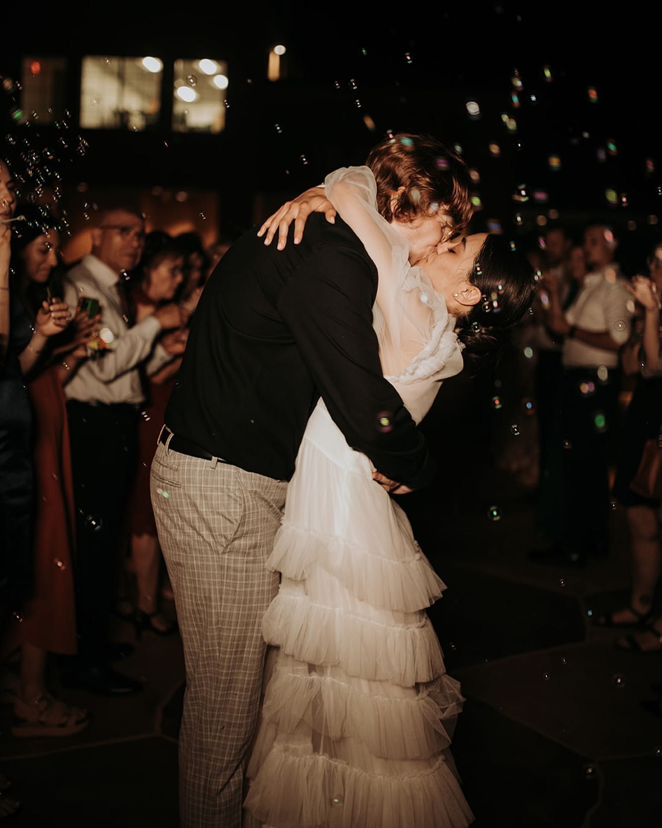 A bride and groom kissing in front of a crowd of people at a wedding reception.
