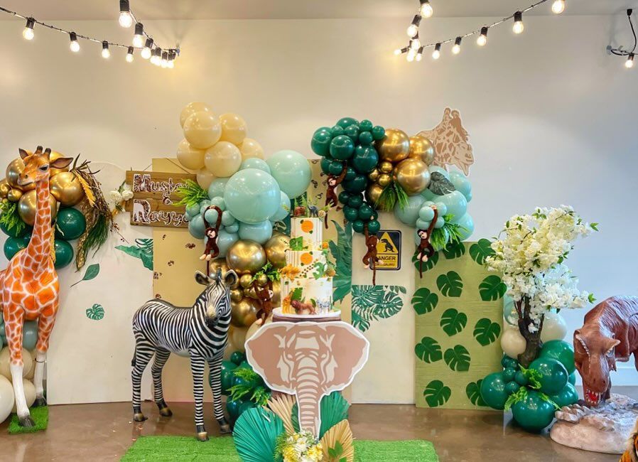 A room decorated with balloons , statues of animals and a cake.