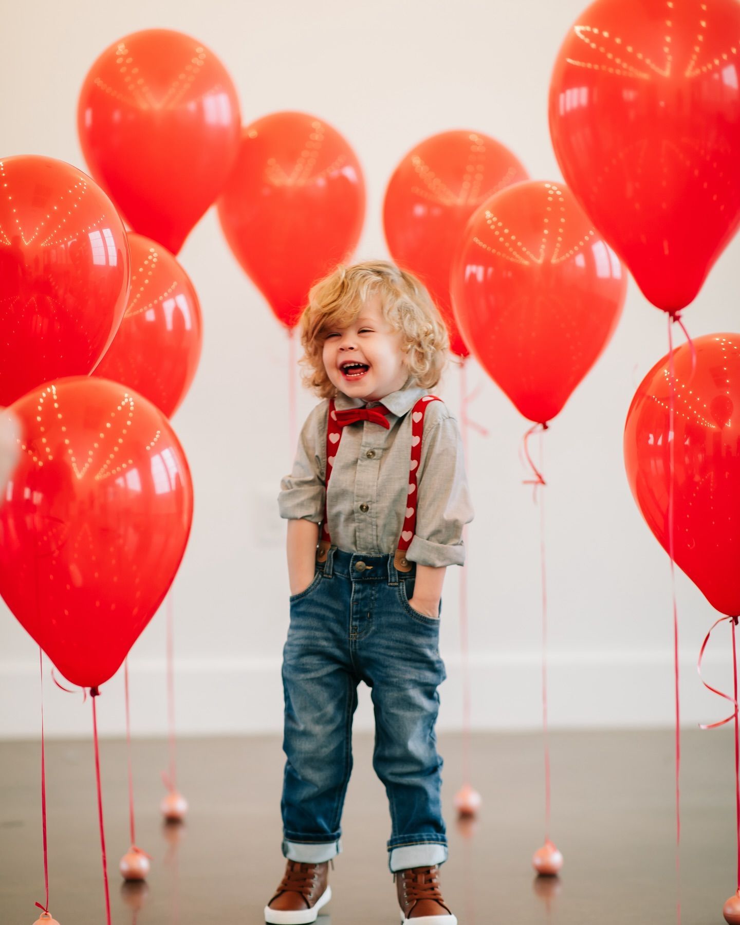 A little boy is standing in front of a bunch of red balloons