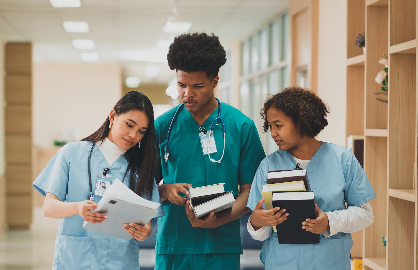 Three medical professionals reviewing documents and books in a hallway.