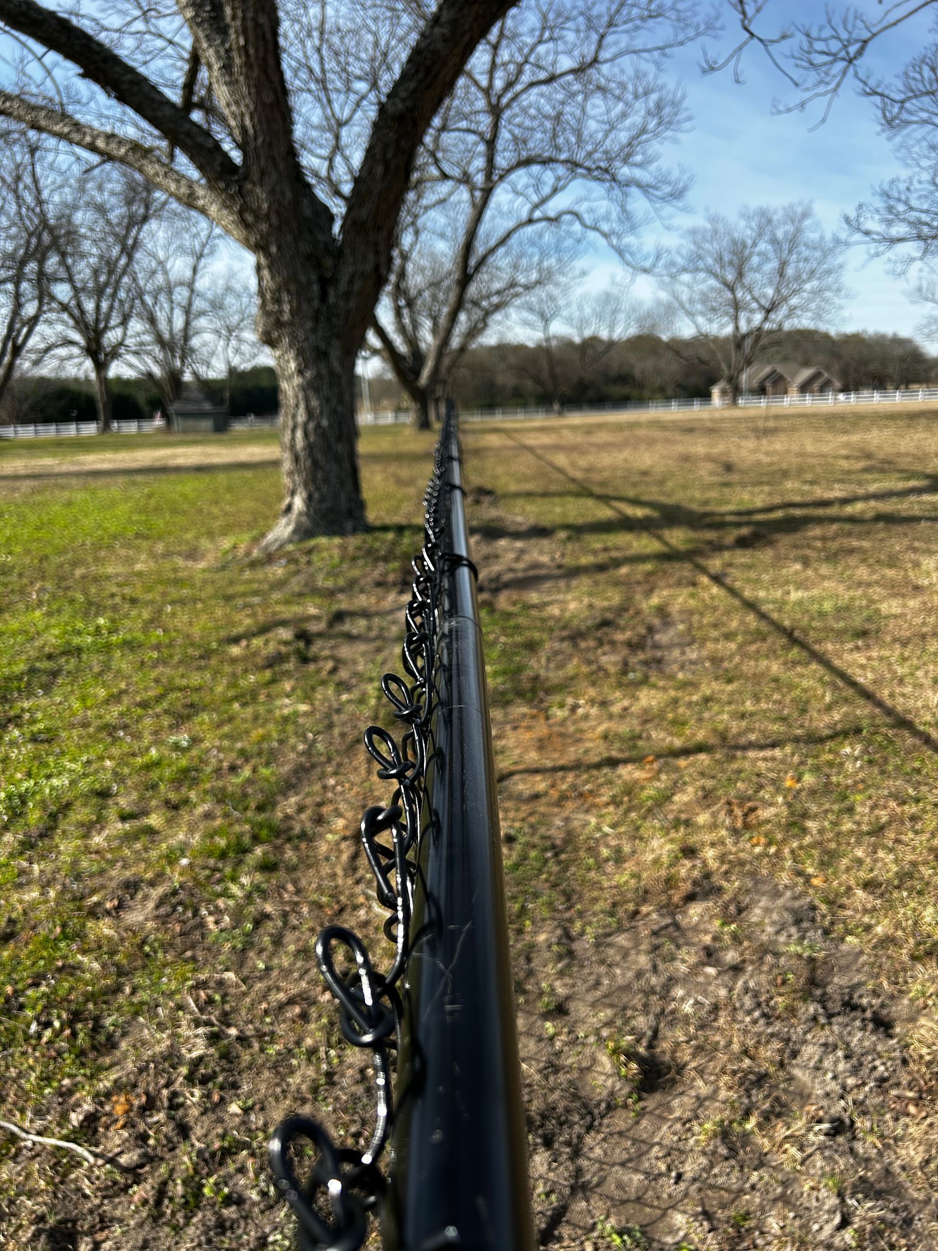 A close up of a fence in a field with trees in the background.
