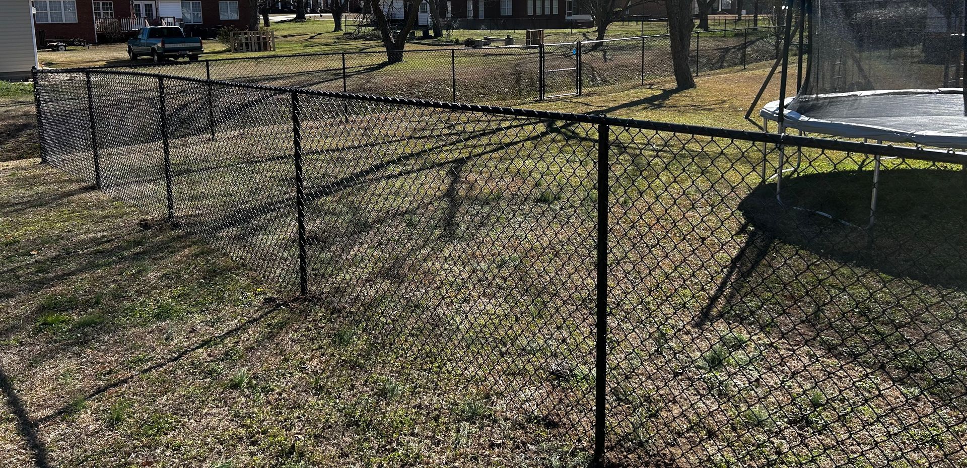 A chain link fence surrounds a trampoline in a yard.