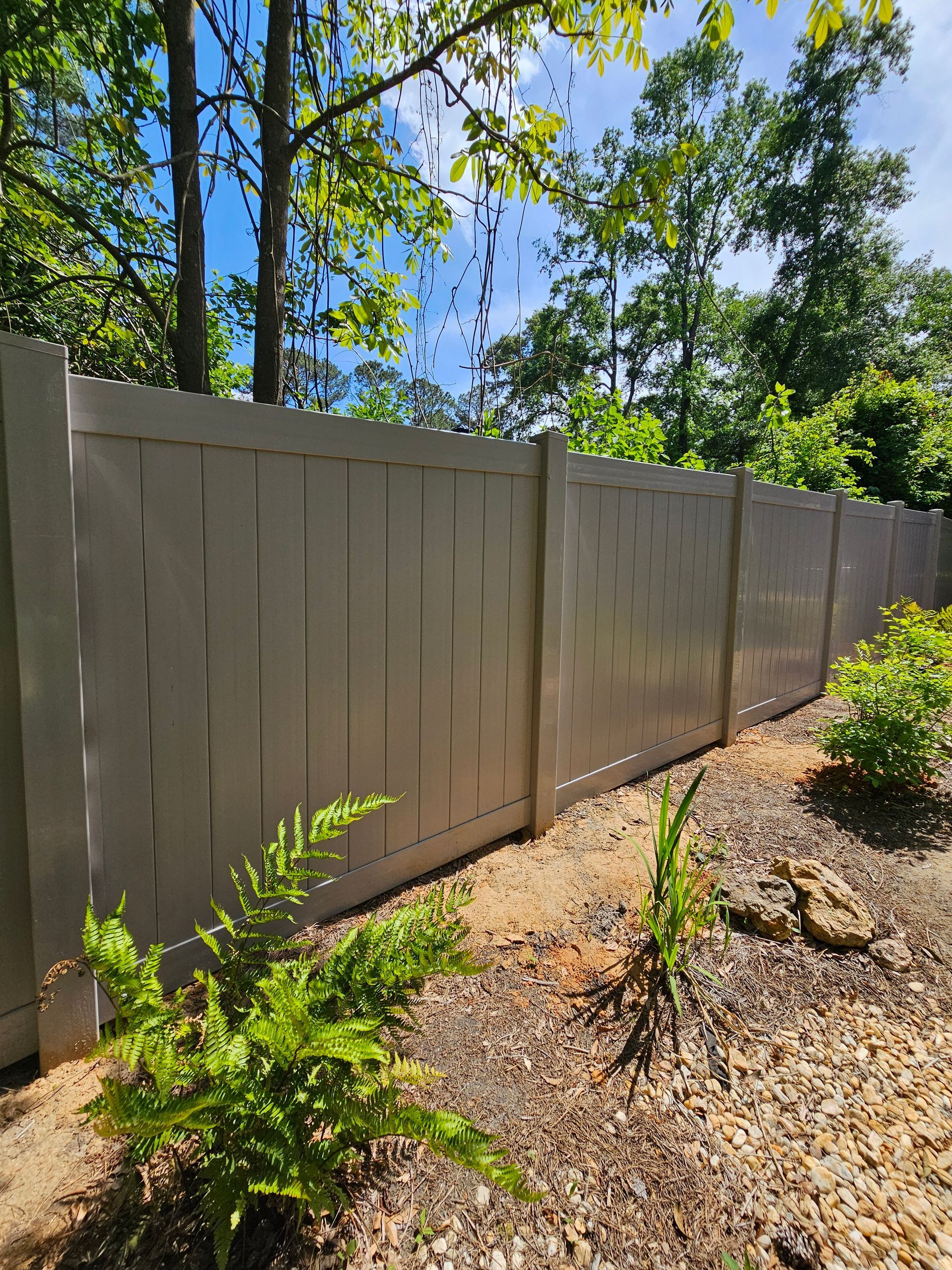 A white fence is surrounded by trees and bushes in a yard.