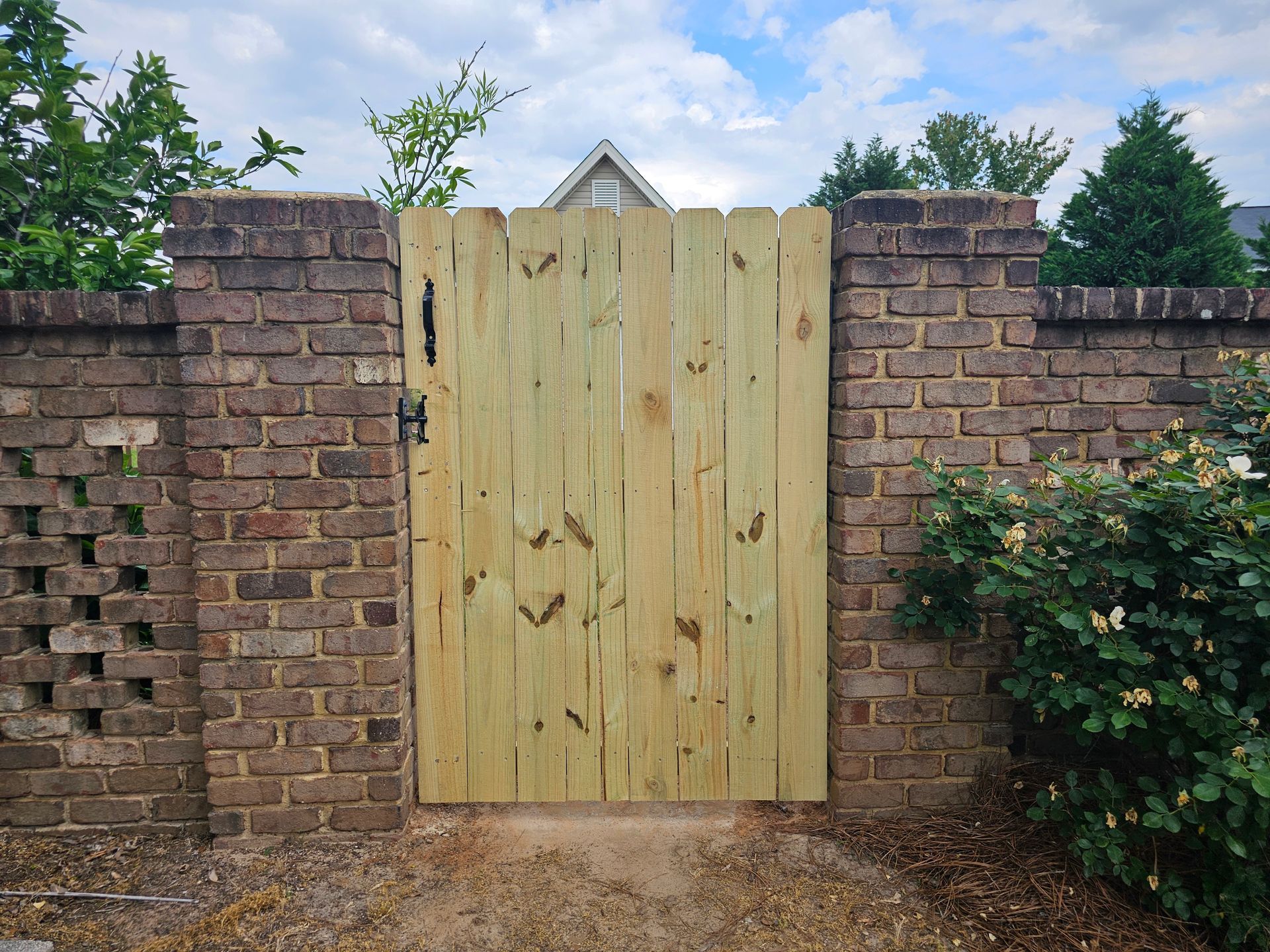 A wooden gate is in front of a brick wall.