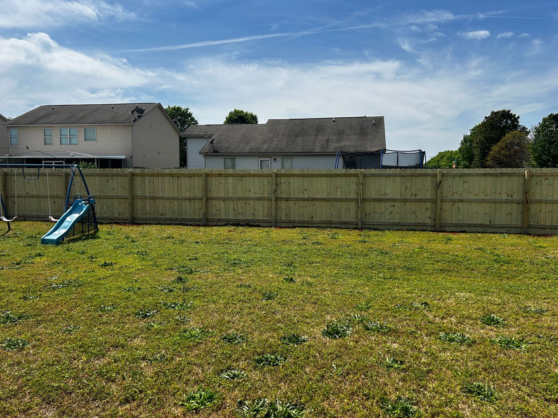 A wooden fence surrounds a grassy yard with a slide in the background.