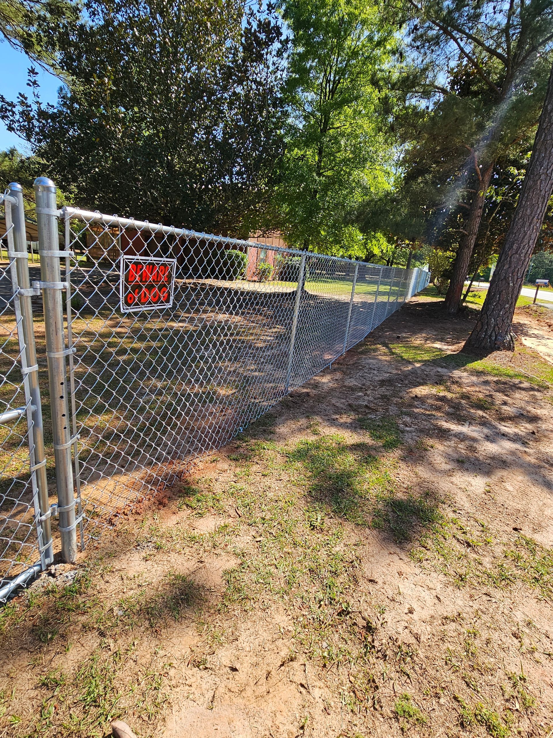 A chain link fence is surrounded by grass and trees in a yard.
